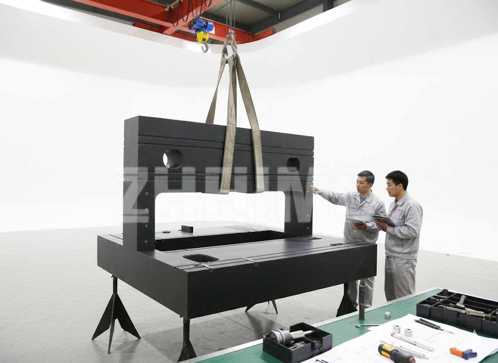 Large granite structural frame with raised portal and T-slots inspected by engineers in the workshop