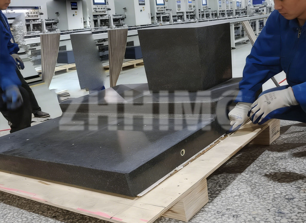 Workshop staff handling a long granite reference part on a wooden pallet before packing